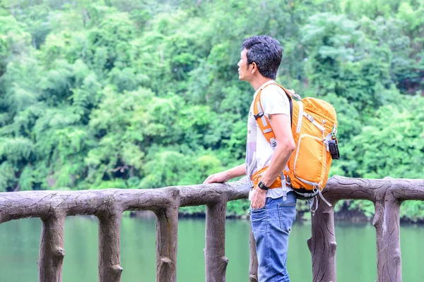 Mężczyzna turysta w dżinsową z pomarańczowy plecak patrząc z widokiem na rzekę — Zdjęcie stockowe