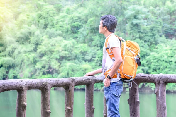 Man hiker in blue jean with orange backpack looking view of river. — Stock Photo, Image