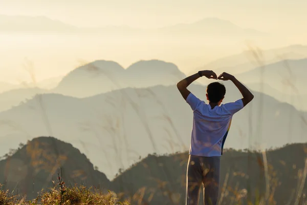 Derrière l'homme se forme une forme de coeur au coucher du soleil avec fond de montagnes en forme de coeur naturel . — Photo