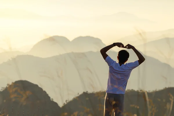 Derrière l'homme se forme une forme de coeur au coucher du soleil avec fond de montagnes en forme de coeur naturel . — Photo