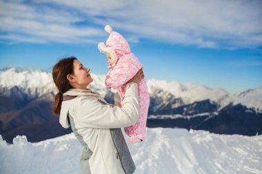 Anne kucağı yeni doğmuş bebeğe karlı yamaçta sarılıyor, mutlu anne kışın güneşli dağda küçük kız çocuğu kucaklıyor, sevgi ve ilgi gösteriyor, annelik izninin tadını çıkarıyor, çocuk bakımı kavramının tadını çıkarıyor. Kopyalama alanı ile