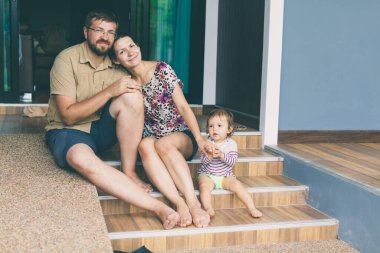 Çocuklu bir aile, verandaya çıkan merdivenlere oturur. Küçük kızlarıyla mutlu ebeveynler özel evlerinin verandasında gülümsüyor ve kameraya bakıyorlar. Emlak kavramı