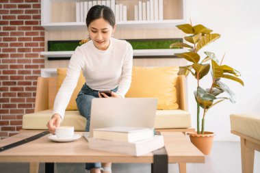 Asyalı kadın kanepede oturuyor ve çalışıyor. Evde dizüstü bilgisayarla çalışan bir iş kadını. Ofiste sakin bir yerde çalışan bir kadın. İş karantina süresi.