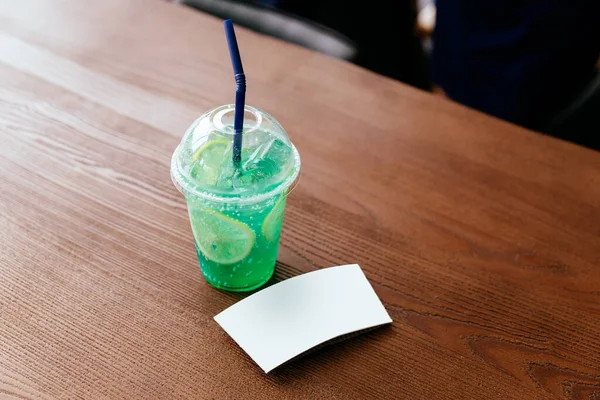 The white cup sleeve of green iced soda with sliced lemon on a wooden table. Cup sleeve template.