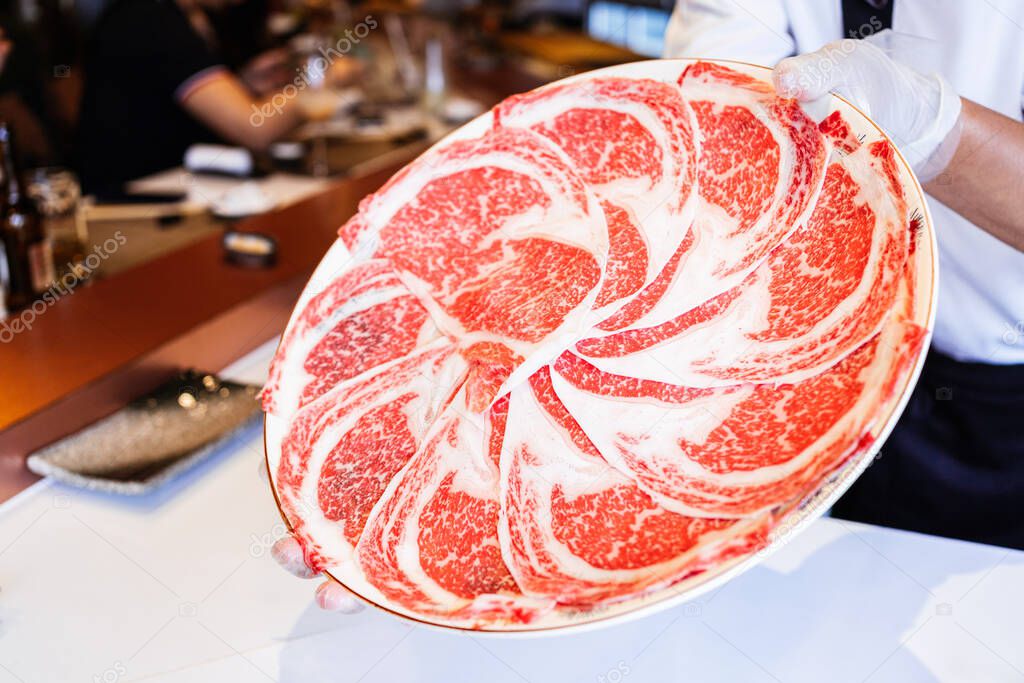 The chef presents Premium Rare Slices Kagoshima Wagyu A5 beef with a high-marbled texture on a circle plate served for Omakase meal. Premium ingredient.