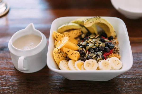 Acai bowl mix with fresh mango, avocado, banana, berries, sunflower seeds, chia seeds and cereal, served with soy milk. Superfood breakfast bowl for healthy and vegan people.