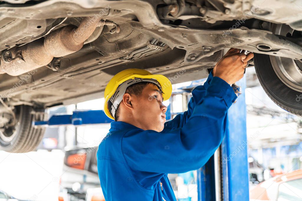 Asian mechanic in blue work wear uniform inspects the car bottom with a wrench with his assistant. Automobile repairing service, Professional occupation teamwork. Vehicle maintenance.