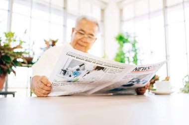 Kıdemli emekli bir adam COVID-19 haberleri hakkında bir gazete okumakla ilgileniyor. Evde kapalı bir bahçede otururken. Emeklilik hobisi ve yaşam tarzı.