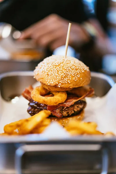 Cheeseburger with medium-rare grilled beef, crunchy bacon, onion rings. Served with onion rings in a stainless steel tray.