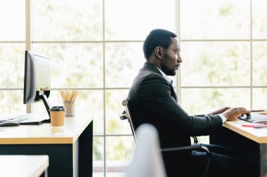 Afrikalı işadamı klavyesini daktilo ediyor ve çalışma masasında fotokopi alanı olan ekrana bakıyor..