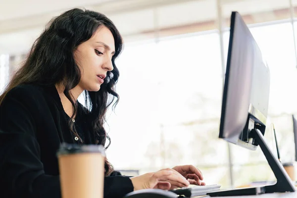 The portrait of a Caucasian businesswoman typing keyboard and looking on keyboard and computer screen with intention at her desk. Concern and fix problems in a corporate office.