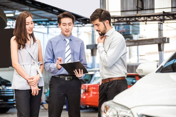 Araba galerisi. Asyalı satıcı (kadın ve erkek) teslim etmeden önce Orta Doğulu müşteri ile listeyi kontrol ediyor. Otomotiv Kiralama ve Satış Şirketi. Uluslararası İş.