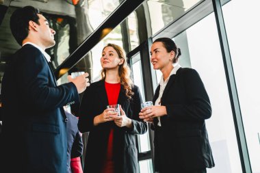 Sunlit ofis lobisinde iş kıyafetleri içinde profesyoneller içki içip sohbet ediyorlar. Sahne satışları, ortaklığı, liderliği, çeşitliliği, planlamayı, semineri ve meslektaşlar arasındaki işbirliğini yansıtıyor