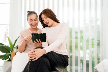 İki kadın kapalı bir evde oturup akıllı telefonu paylaşıyor, bir kanepede gülümsüyor ve rahat bir şekilde bitkilerle birlikte evde vakit geçiriyorlar..