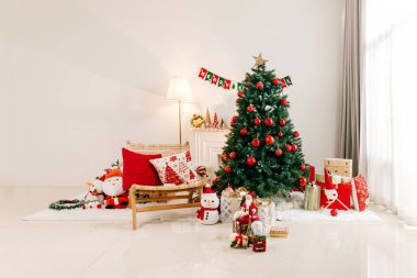 Noel için dekore edilmiş rahat oturma odası: süslerle süslenmiş kırmızı-yeşil bir ağaç, hediye paketleri, şenlikli yastıklar ve lamba ve pencerenin yanında tatil figürleri..