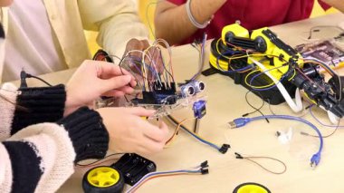 Birkaç el, elektronik ve robot projesi sırasında kabloları, sensörleri ve mikro kontrolörleri birbirine bağlayan küçük tekerlekli bir robotu bir masanın üzerinde birleştirir..