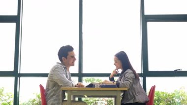 Masanın karşısındaki kütüphanede oturan iki kişi, masada kitaplarla arkadaşça bir tartışmaya giriştiler. Çalışma öneriyorlar ya da parlak bir öğrenim alanında toplantı öneriyorlar..