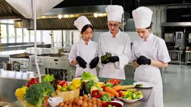 Profesyonel bir aşçılık kursunda taze sebzelerle iki genç aşçılık öğrencisine yemek öğretiyor. Aşçılık eğitimi, gastronomi ve gıda eğitimi konuları için ideal..