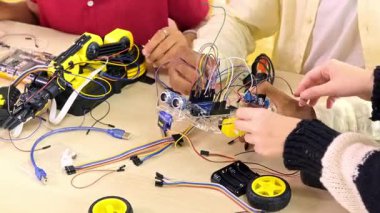 Birkaç el, elektronik ve robot projesi sırasında kabloları, sensörleri ve mikro kontrolörleri birbirine bağlayan küçük tekerlekli bir robotu bir masanın üzerinde birleştirir..