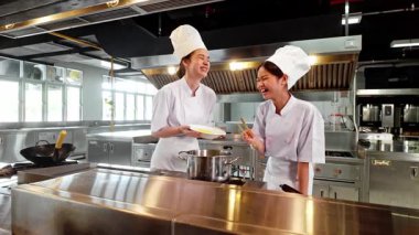 Beyaz üniformalı ve şapkalı iki şef, şık, modern bir mutfakta fırında yemek pişirirken, profesyonel bir ortamda aşçılık uzmanlığı, takım çalışması ve yemek hazırlama konusunda işbirliği yapıyorlar..