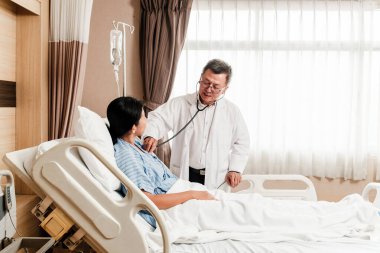 Bir sağlık uzmanı, hastane odasında bir hastayı muayene etmek için steteskop kullanır. Klinik bakım, güven ve profesyonel hizmeti temiz ve modern bir tıbbi ortamda vurgular..