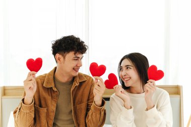 Neşeli bir çift, sıcak, samimi bir ortamda, sevgi, birlik ve gerçek bir sevgi ifade eden kırmızı kalp şekillerini tutarken yürekten bir gülümsemeyi paylaşır. Sevgililer Günü ve yaşam tarzı markaları için mükemmel.