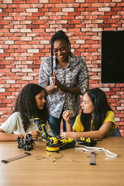 İki kız bir robotik projesinde birlikte çalışırken bir yetişkin onlara modern ve yaratıcı bir sınıf ortamında rehberlik ediyor..