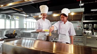 Beyaz üniformalı ve şapkalı iki şef, şık, modern bir mutfakta fırında yemek pişirirken, profesyonel bir ortamda aşçılık uzmanlığı, takım çalışması ve yemek hazırlama konusunda işbirliği yapıyorlar..