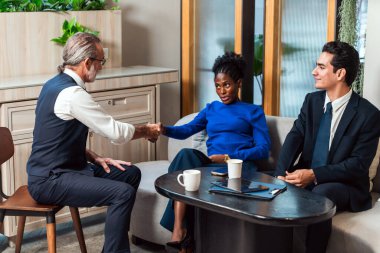 Modern bir ortamda işbirliği ve iş etkileşimine vurgu yapan, sohbet eden ve el sıkışan üç kişinin olduğu profesyonel bir toplantı sahnesi..