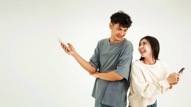 İki genç arkadaş arka arkaya gülüyor ve akıllı telefonları parlak bir stüdyoda tutuyorlar, neşeli bir anı ve sosyal bağlantıyı paylaşıyorlar..