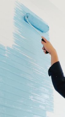 Boya silindiri kullanan el, bir ev yenilemesi sırasında beyaz bir gemi duvarına açık mavi boya uygular.