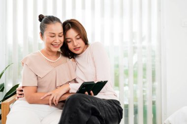 İki kadın kanepede birlikte oturur, gülümser ve küçük bir kitap okurlar. Dikey perdeleri olan, sıcak, rahat bir anı evde paylaşırlar..