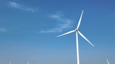 Modern bir rüzgar türbini temiz, yenilenebilir enerji üretimini sembolize eden açık mavi bir gökyüzüne karşı duruyor..