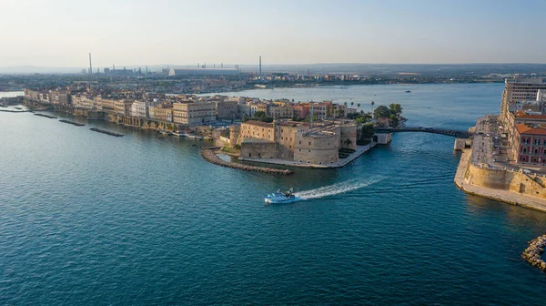 Taranto, Puglia (Apulia), İtalya. İHA 'dan Toranto Körfezi' ni geçen küçük bir gemiye kadar uçan güzel panoramik hava manzaralı fotoğraf. Arka planda deniz kanalında eski ortaçağ Aragonese Kalesi, günbatımında eski Taranto şehri,)