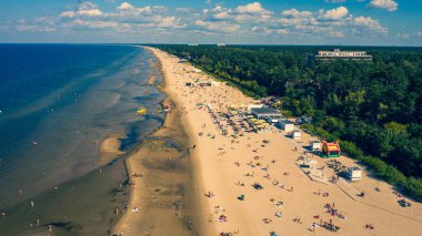 Dzintari, Jurmala, Letonya, Baltık. Sıcak ve güneşli bir yaz gününde Baltık Denizi 'nde güneşlenen ve yüzen insanlarla dolu Dzintari kumlu plajına uçan dron panoramiklerinden havadan çekilmiş bir fotoğraf. (Seriler)