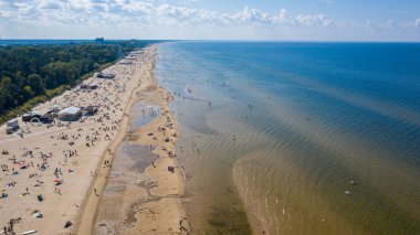 Dzintari, Jurmala, Letonya, Baltık. Sıcak ve güneşli bir yaz gününde Baltık Denizi 'nde güneşlenen ve yüzen insanlarla dolu Dzintari kumlu plajına uçan dron panoramiklerinden havadan çekilmiş bir fotoğraf. (Seriler)