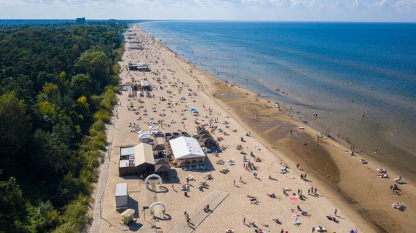 Dzintari, Jurmala, Letonya, Baltık. Sıcak ve güneşli bir yaz gününde Baltık Denizi 'nde güneşlenen ve yüzen insanlarla dolu Dzintari kumlu plajına uçan dron panoramiklerinden havadan çekilmiş bir fotoğraf. (Seriler)