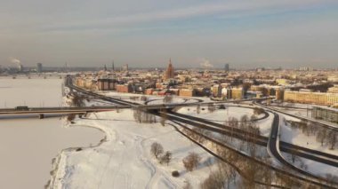 Riga, Letonya, Baltık. Uçan İHA 'dan hareket eden makinelerle Ada Köprüsü' ne, kış günbatımından güzel panoramik 4K video. (Seriler)