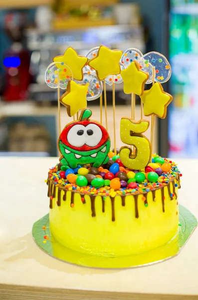 delicious yellow cake for the birthday of a 5-year-old child, yellow stars and transparent candies on the cake, the number 5 and a green figure