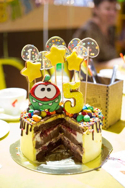 yellow chocolate cake cut into pieces on the birthday of a 5-year-old child, yellow stars and transparent candies on the cake, the number 5 and the green number. A piece of cake is cut off.