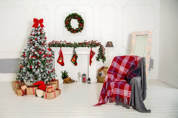 new year\'s interior in a loft room with a green decorated pine tree, a chair and a warm red blanket.