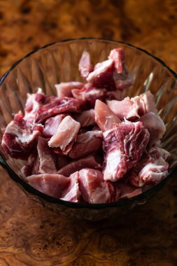 Cam bir kasede, ahşap bir masada duran taze, çiğ et. Bu görüntü, etin dokusuna odaklanarak yemek pişirmek için gerekli malzemelerin hazırlanmasını yakalar..