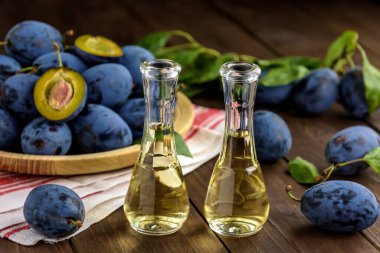 Erik brendisi ya da küçük cam şişelerde Schnapps ve ahşap bir masada taze ve lezzetli erikler. Seçici odak.