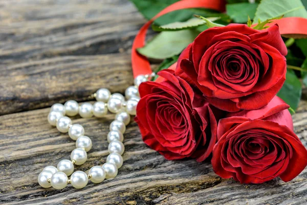 Three red roses and string of pearls on a old wooden table with copy space for text. Selective focus.