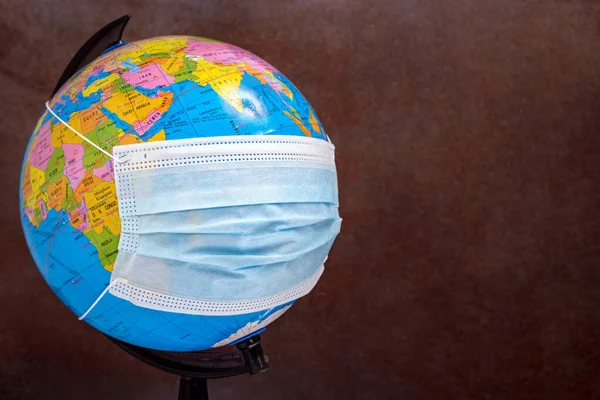 Earth globe with surgical face mask. The concept of the global problem of corona virus prevention and treatment, travel during a pandemic. Selective focus.