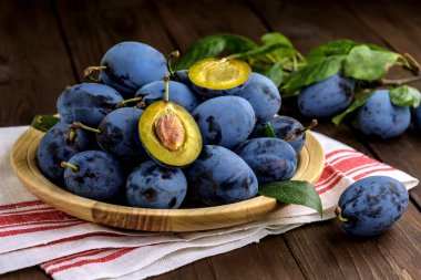 Kahverengi masada bulaşık bezi olan ahşap bir tabakta tatlı erikler. Seçici odak.