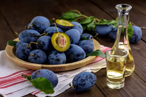 Erik brendisi ya da küçük cam şişelerde Schnapps ve ahşap bir masada taze ve lezzetli erikler. Seçici odak.