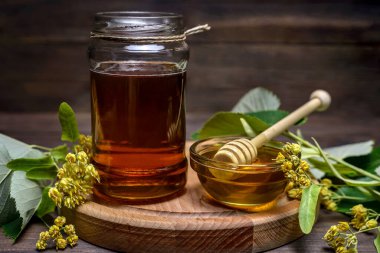 Kavanoz ve ıhlamur balı bal ve bal için sopa ve ahşap bir masada taze ıhlamur çiçeği..