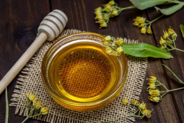 Ballı cam kase, bal için sopa ve ahşap bir masada taze ıhlamur çiçeği. Seçici odak.