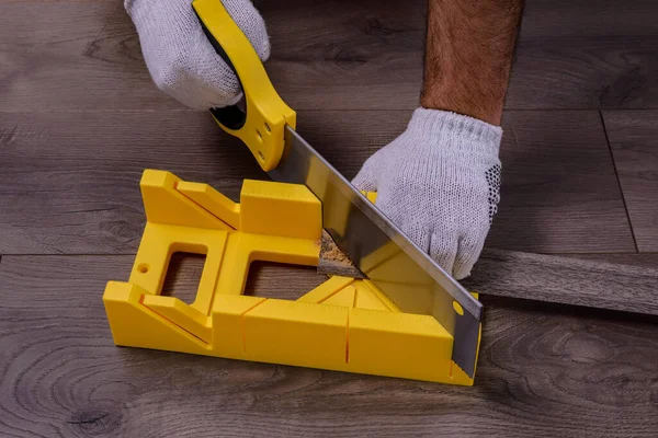 Bir adam testereyle etek tahtasını kesiyor ve plastik zemin üzerinde yelkenli kutusu var..